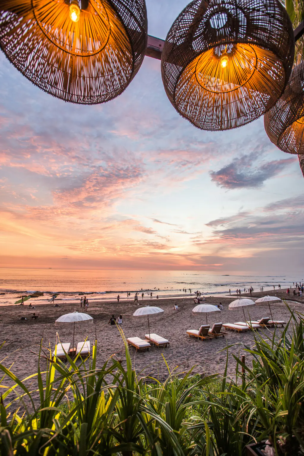 Woven lanterns glowing over the beach at sunset, loungers on the sand