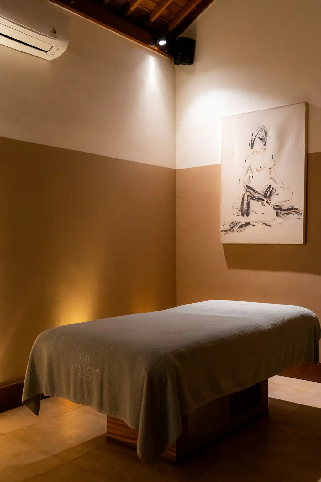 A softly lit spa room with a treatment bed and a Balinese sketch on the wall